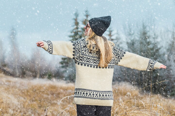 Wall Mural - Outdoor close up portrait of young beautiful woman with long hair wearing hat, sweater posing in nature view. Christmas, winter holidays concept. Snowfall. Snow trees on background.