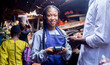 © wazkkii - shot of young African friendly saleswoman passing pos terminal over counter to customer paying with smartphone using wireless transfer
