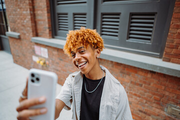 Wall Mural - Young dark-skinned man posing at the street and taking selfie in the city background