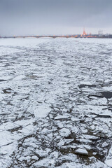 Wall Mural - Winter view of the Neva River and the historical center of St. Petersburg. Cracked ice floes on the water surface. In the distance Trinity Bridge and Peter and Paul Cathedral. Cold weather. Russia.