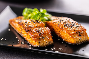 Wall Mural - Two salmon fillets baked until crispy, sprinkled with sesame on a black plate.