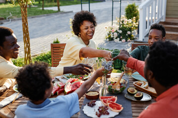 Wall Mural - Portrait of smiling young woman clinking glasses with family and friends while enjoying dinner outdoors