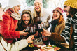 © Davide Angelini - Happy friends group toasting red wine dining at restaurant terrace - Young people socializing drinking and eating food sitting outside at winery bar table - Winter season - Dinner lifestyle concept