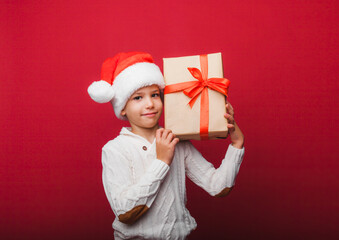 Cute little boy in a Santa Claus hat holding a gift box on a red background. a child with a New Year's gift for Christmas. new year