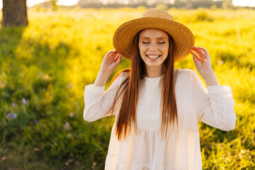 Wall Mural - medium shot portrait of pretty laughing young woman in straw hat and white dress standing posing wit