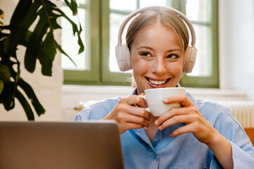 Wall Mural - White young woman drinking coffee while working with laptop at cafe