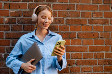 Wall Mural - Young white woman in headphones listening music while using cellphone