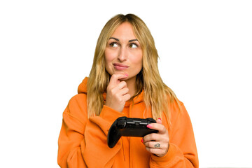 Young caucasian gamer woman holding a game controller isolated on green chroma background looking sideways with doubtful and skeptical expression.