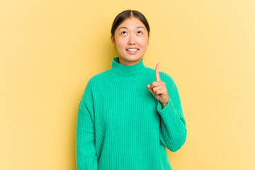 Wall Mural - Young Asian woman isolated on yellow background indicates with both fore fingers up showing a blank space.