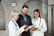 © Goran - Two doctors and mid adult businessman working on digital tablet in the office.