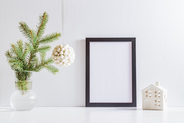 Mock up poster frame with christmas decoration in home interior, scandinavian style. Green fir branches in a vase on a white table