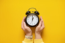 Daylight Saving Day. Fall Back. Black Alarm Clock And Female Hands On Yellow Background. Daylight Saving Time End