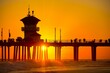 Silhouette of a pier with walking people under an orange sunset sky on Huntington Beach, California