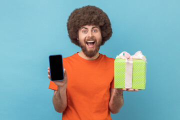 Wall Mural - portrait of excited amazed man with afro hairstyle wearing orange t-shirt standing with present box 