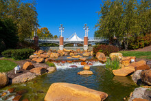 A Gorgeous Autumn Landscape At World's Fair Park With A Flowing River With Green Water Rushing Over Smooth Brown Rocks Surrounded By Autumn Colored Trees And Lush Green Trees And Grass In Knoxville