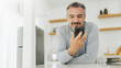 © eggeeggjiew - Mature Adult man using mobile phone or smartphone in kitchen at home.