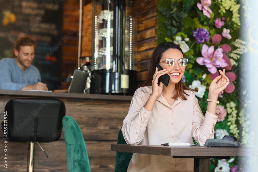 Beautiful business owner talking by mobile phone at table in her cafe