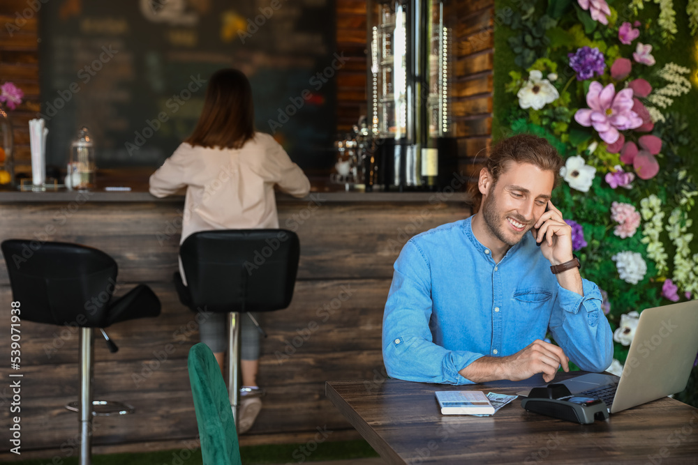 Handsome business owner talking by mobile phone at table in his cafe
