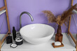 Modern sink and different bath accessories near color wall in bathroom