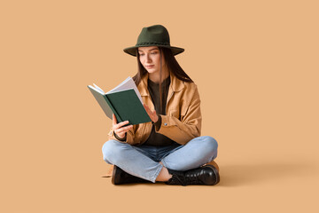 young woman in hat reading book on beige background