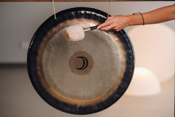 Close-up of a woman's hand pounding a gong with a hammer. Gong and hand beater for gong