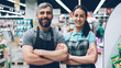 © silverkblack - Portrait of two supermarket employees attractive young people in aprons standing inside shop, smiling and looking at camera. Shelves with food and drinks are visible.