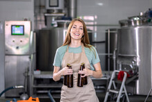 Portrait Of Female Brewer In Craft Brewery Holding A Beer Bottle.