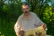 nice outdoor portrait of Ukrainian peasant taking frame with bees while hard working in own bee yard