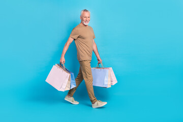 Poster - Full body profile photo of positive person hold packages walking isolated on blue color background