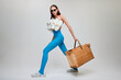 Portrait of young beautiful girl posing in blue tights, paper bag and top made from slippers isolated on grey background. High fashion