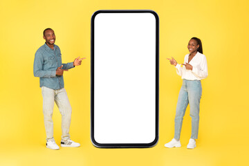 Black Couple Showing Large Phone Screen Pointing Fingers, Yellow Background