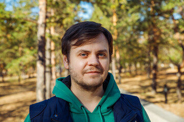 Looking at camera smiling young 34 years old caucasian unshaven beard man in autumn Park or forest. Headshot man lifestyle portrait. Healthy lifestyle concept.