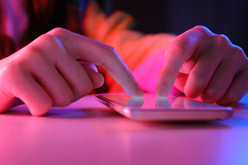 Use of mobile phone in trendy neon lights. Creative vivid color of ultraviolet red and blue. Hands of Teen Girl scrolling up photos Close-up at dark neon room. App for sale in shop, Social media.