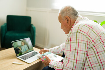 Wall Mural - Rear view of an ill old man talking with a virtual doctor