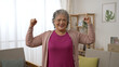© PRPicturesProduction - front portrait of a strong healthy asian senior old female looking at the camera with a  smile while showing her shoulder muscles in the living room at home.