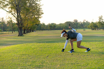 Wall Mural - Asian sporty woman putt golf ball on tee off with club in golf course on evening on time for healthy sport sunset background. Lifestyle and Sport Concept