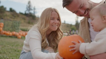 close up of mom handing pumpkin to toddler, young family at pumpkin patch