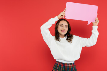 Wall Mural - positive brunette woman holding speech bubble and looking at camera on red background