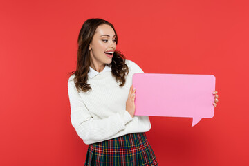 Canvas Print - Happy woman in sweater looking at empty speech bubble isolated on red