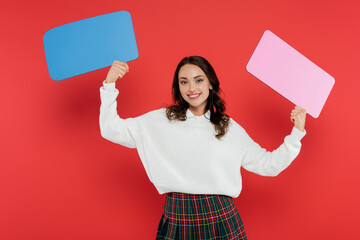 Wall Mural - cheerful woman in cozy sweater holding speech bubbles on red background