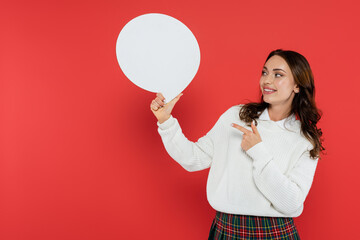 Wall Mural - smiling woman in cozy sweater pointing at speech bubble on red background