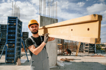 Front view. Carrying wooden plank. Man in uniform is working on the construction site