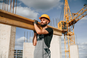 Holding and walking with wooden plank. Man in uniform is working on the construction site