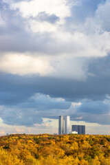 Wall Mural - large rainy cloud over yellow autumn forest and skyscrapers on horizon on sunny day