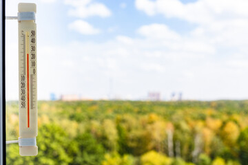 Wall Mural - thermometer on window glass on warm autumn day and colorful city park outside window (focus on the t