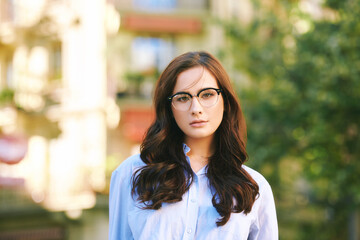 Wall Mural - Outdoor portrait of pretty young woman with dark hair, wearing eyeglasses