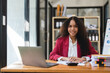 © Natee Meepian - Black Businesswoman Sitting at Her Desk Working on a Laptop Computer. Smiling Successful African American Woman working with Big Data e-Commerce