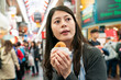 © PR Image Factory - closeup of asian female tourist holding doughnut and looking into distance while searching for direction in crowded kuromon ichiba market in Osaka japan
