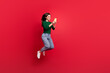 © deagreez - Full length photo of cheerful excited girl jumping using gadget social media wear stylish green clothes isolated on shine red color background