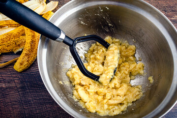 Wall Mural - Mashed Banana in a Large Mixing Bowl: Mashed bananas and a potato masher in a metal mixing bowl